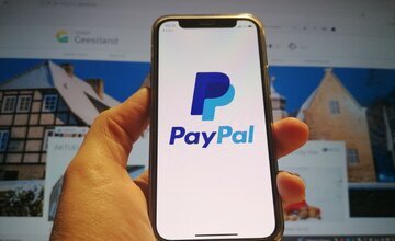 Smartphone mit PayPal-Logo vor Bildschirm, der Geestland-Homepage anzeigt