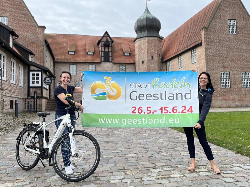 Dana Hebener und Sonja Thomas mit STADTRADELN-Plakat vor der Burg Bederkesa