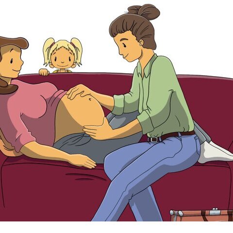 Hebamme sitzt mit schwangerer Frau auf einem Sofa und tastet den Bauch ab