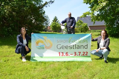 Sonja Thomas, Thorsten Krüger und Dana Hebener stehen mit einem STADTRADELN-Banner auf einer grünen Wiese