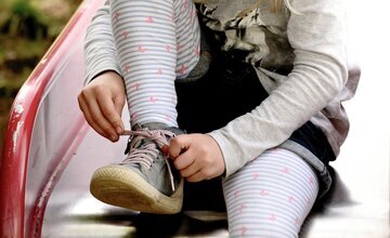 Kind bindet sich die Schuhe zu
