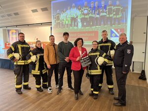 Feuerwehrkameraden und Bürgermeisterin vor der Leinwand im Lindenhofsaal