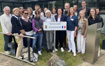 Vertreterinnen und Vertreter aus Geestland und Roquevaire stehen am neuen Schild am Langener Rathaus