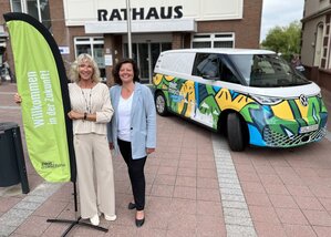 Projektleiterin Britta Murawski und Bürgermeisterin Gabi Kasten neben einem bunt beklebten VW ID.BUZZ